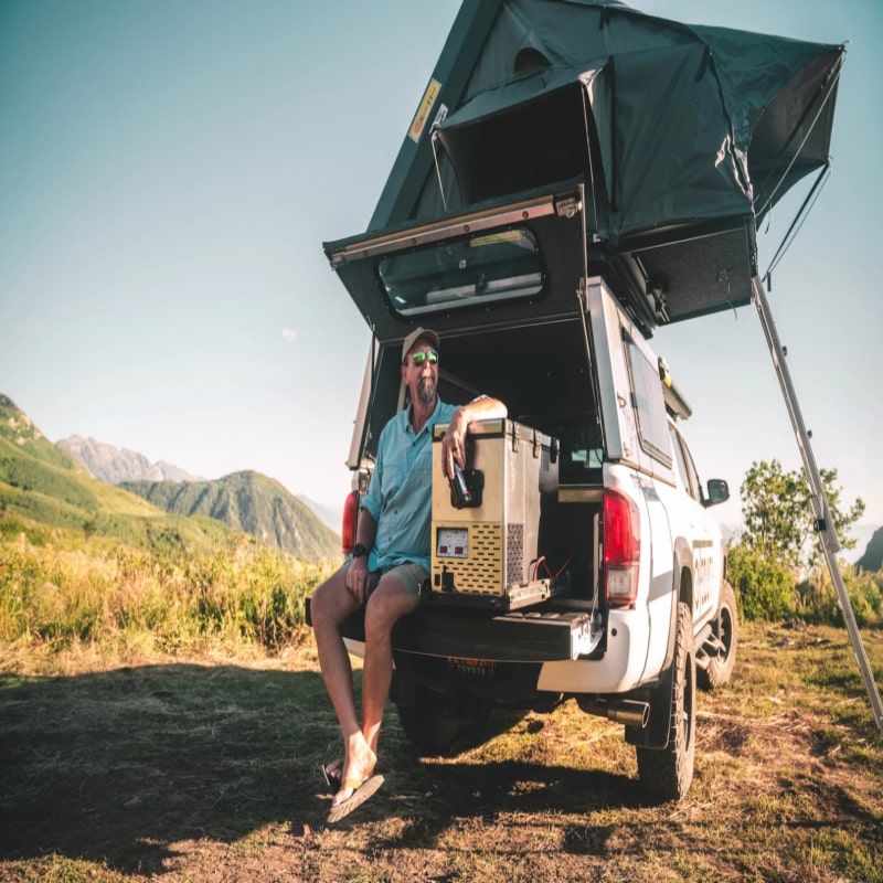 National luna 35l mini fridge outside in truck with roof top tent and camper having a drink